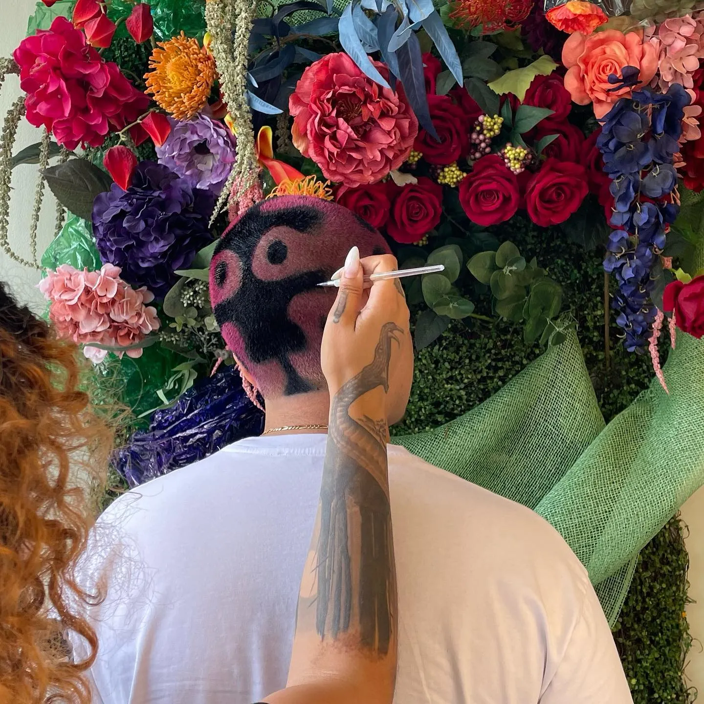 Floral hair design being painted in front of a flower wall